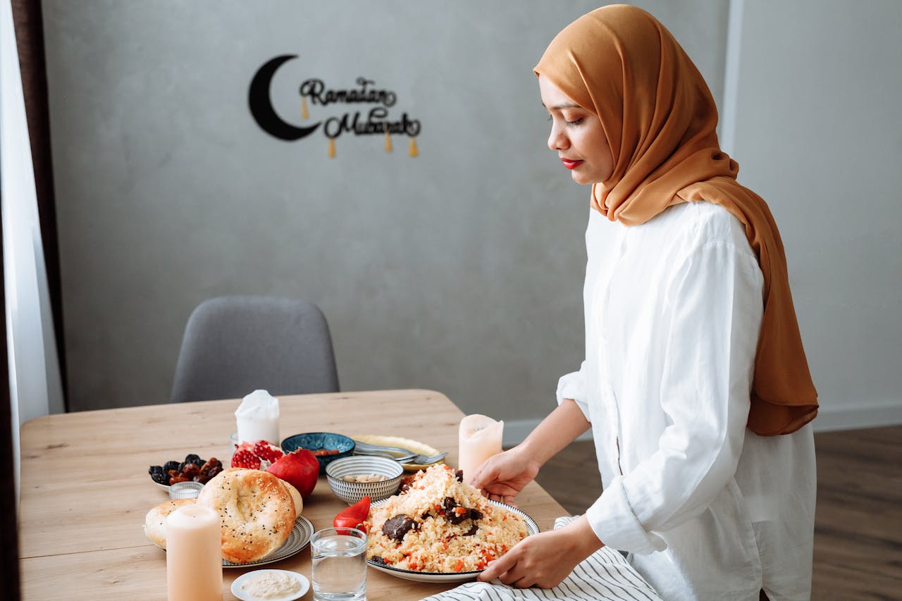 Muslim woman in hijab setting table with traditional iftar food during Ramadan.
